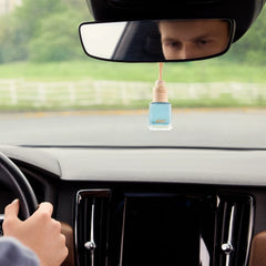 An fresh Airpro cool tide glass bottle car diffuser with a wooden cap hanging from a car rearview mirror during a daylight drive.