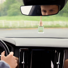 An Airpro Jade Tea glass bottle car diffuser with a wooden cap hanging from a car rearview mirror during your drive.