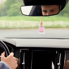 An Airpro floral Sakura Lumi glass bottle car scent with a wooden cap hanging from a car rearview mirror during a drive.